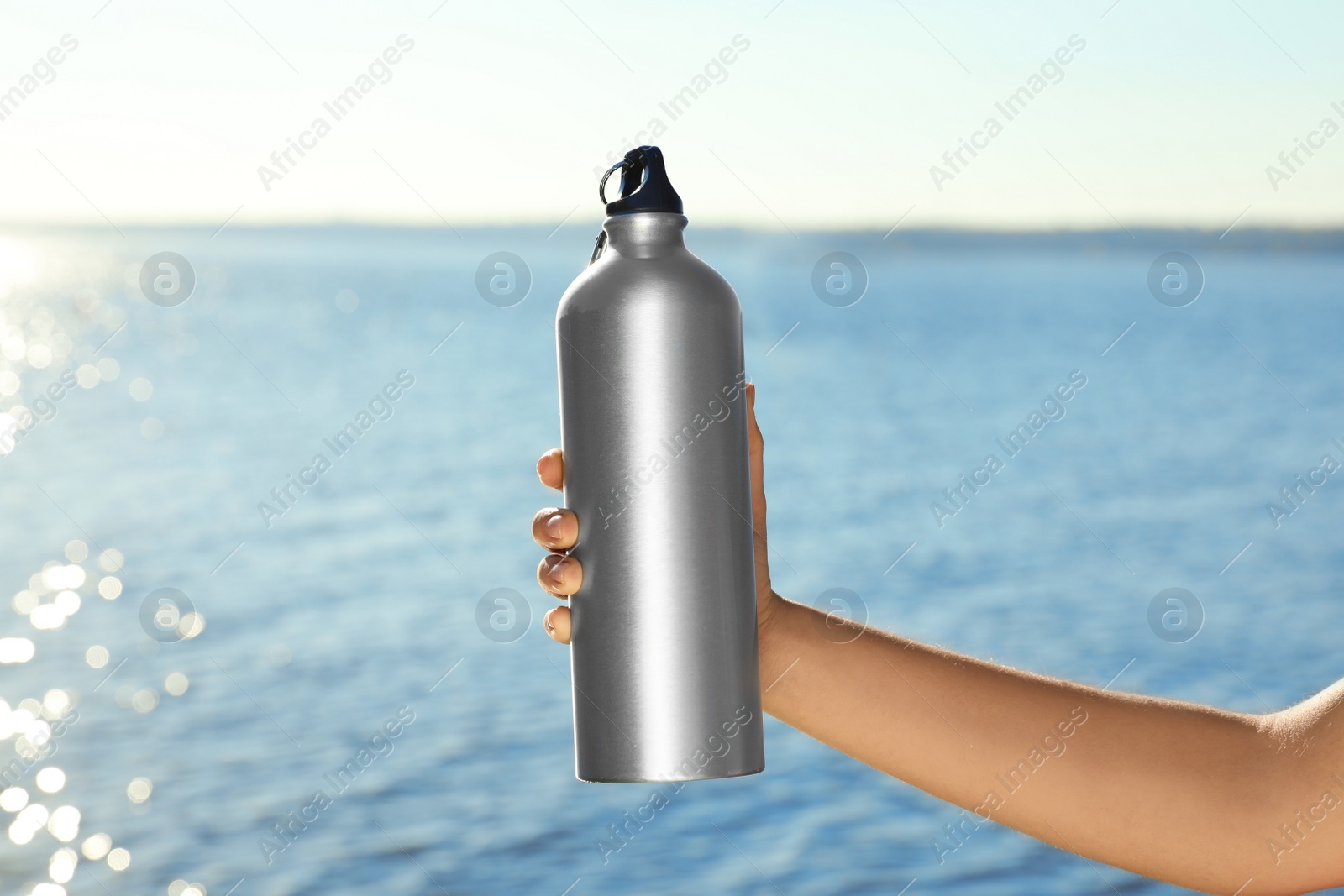 Photo of Young sporty woman holding water bottle near river on sunny day