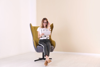 Photo of Young woman with tablet sitting in armchair at home. Space for text