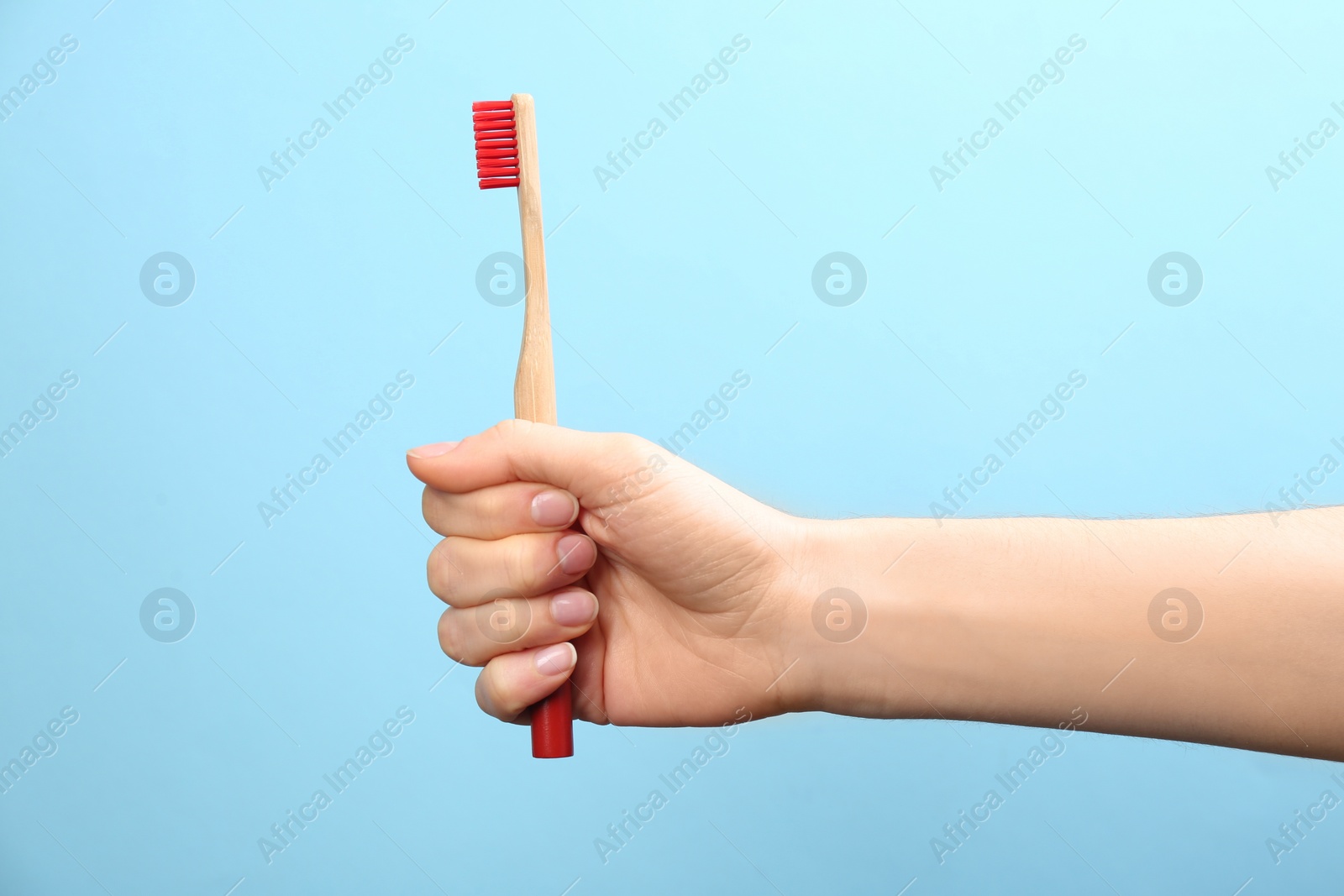 Photo of Woman holding bamboo toothbrush on light blue background, closeup