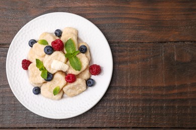 Photo of Plate of tasty lazy dumplings with berries, butter and mint leaves on wooden table, top view. Space for text