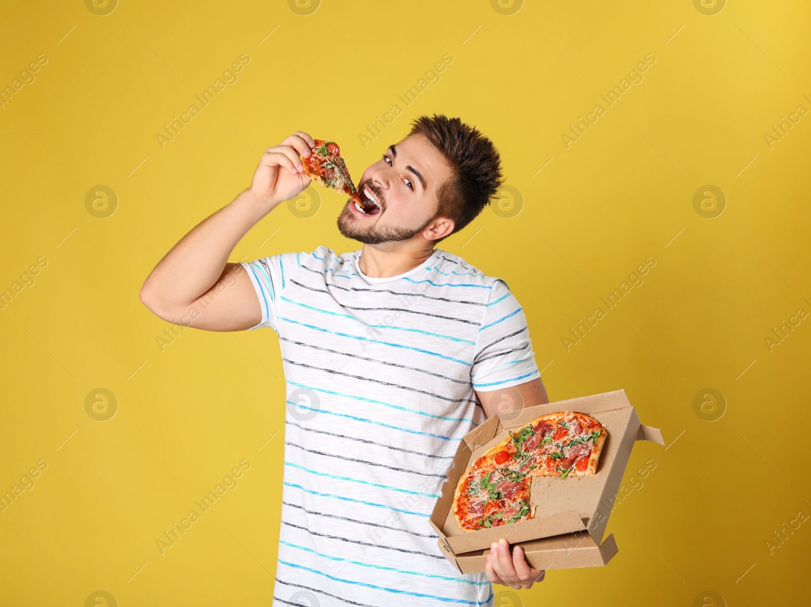 Photo of Handsome man eating tasty pizza on yellow background