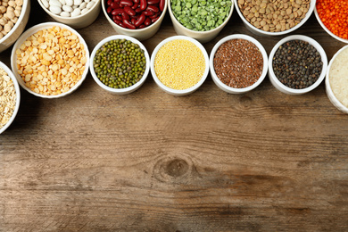 Photo of Different grains and cereals on wooden table, flat lay. Space for text