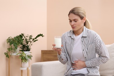 Photo of Woman with glass of milk suffering from lactose intolerance at home, space for text