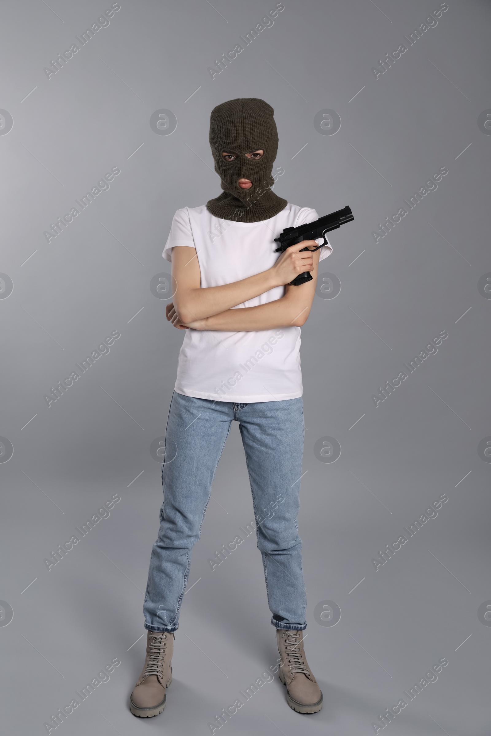 Photo of Woman wearing knitted balaclava with gun on grey background