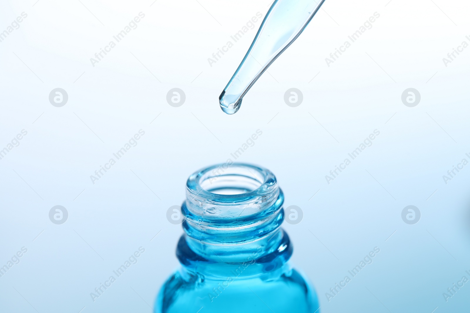 Photo of Dripping liquid from pipette into glass bottle on light blue background, closeup