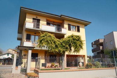 Beautiful house with metal fence and green tree on sunny day