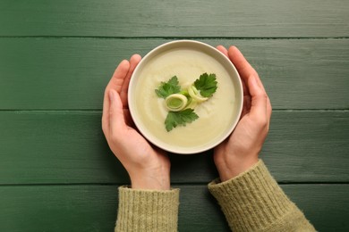Photo of Woman holding bowl of delicious leek soup at green wooden table, top view