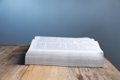 Photo of Closeup view of open Bible on wooden table against grey background, space for text. Religious book