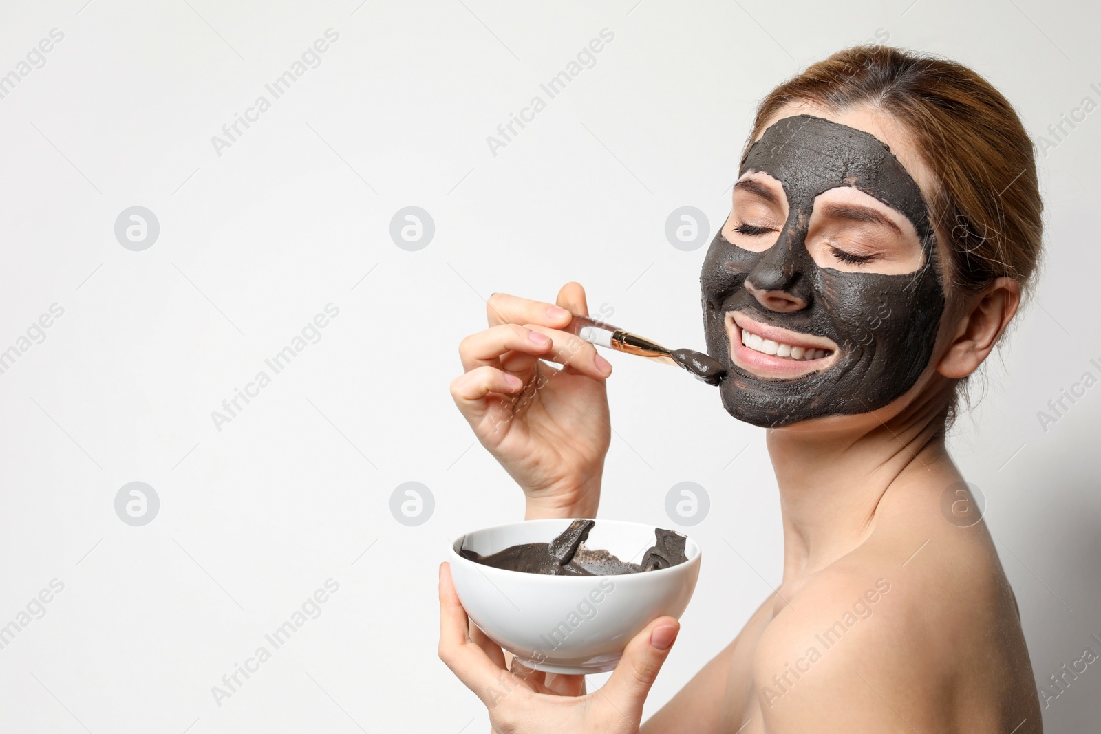 Photo of Beautiful woman applying black mask onto face against light background. Space for text