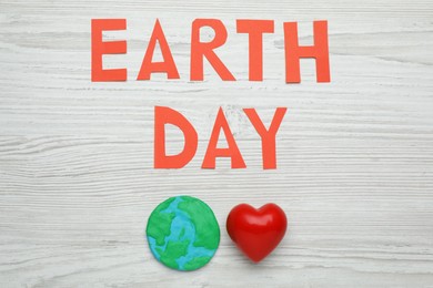 Photo of Words Earth Day, plasticine planet and decorative heart on white wooden table, flat lay