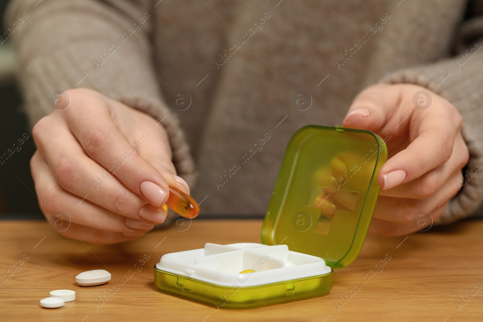 Photo of Woman taking pill from plastic box at wooden table, closeup