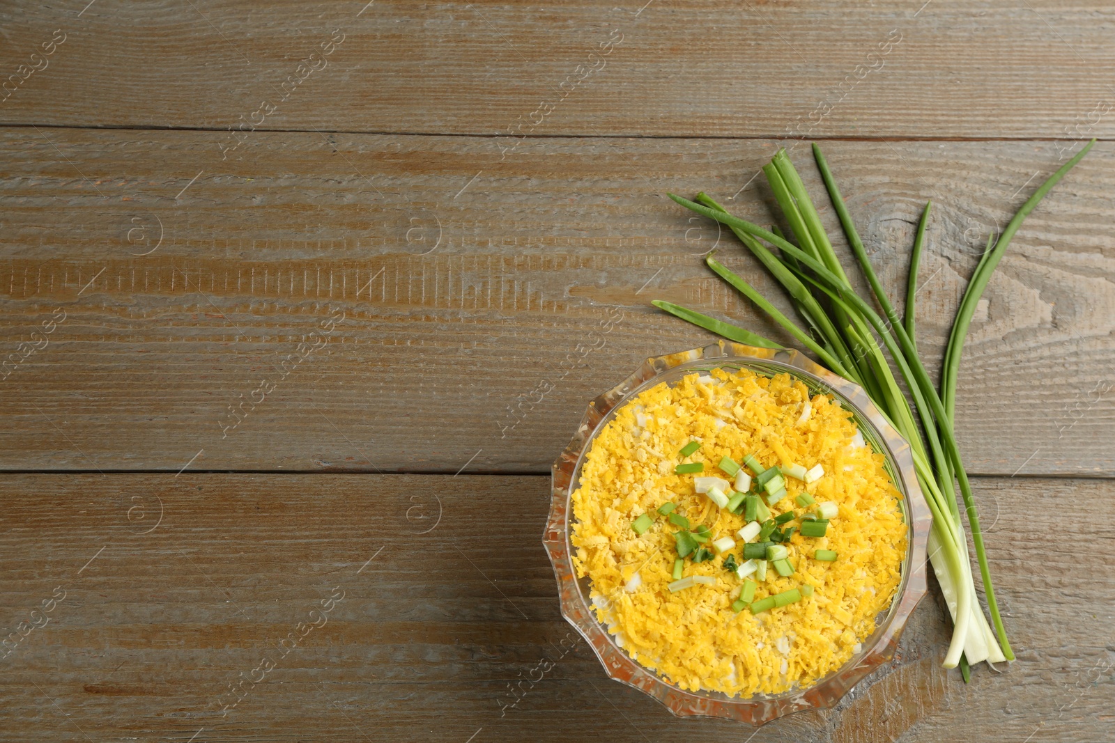 Photo of Traditional russian salad Mimosa and green onion on wooden table, flat lay. Space for text