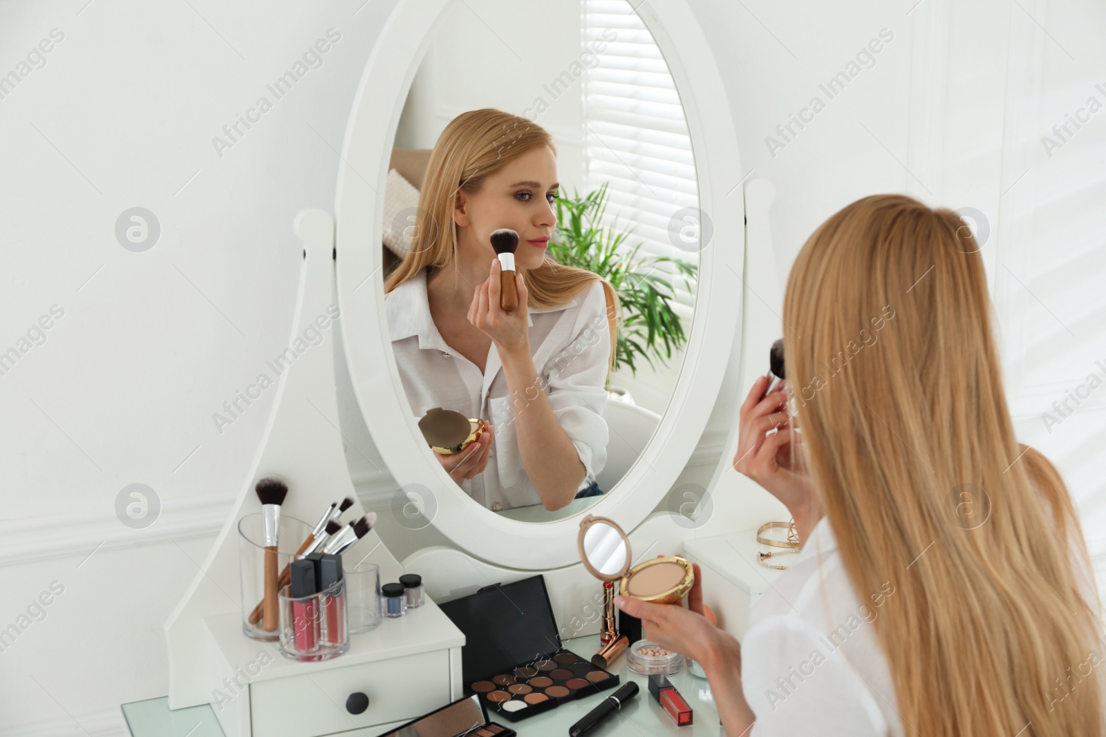 Photo of Beautiful woman applying makeup near mirror in room