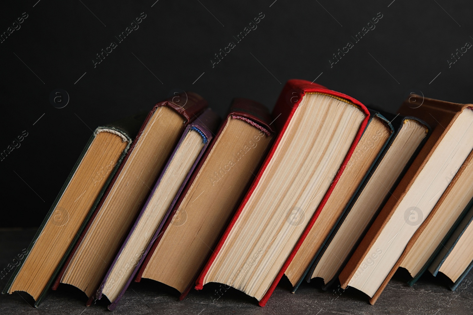 Photo of Stack of hardcover books on grey stone table against black background