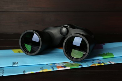 Photo of Modern binoculars and map on wooden table, closeup