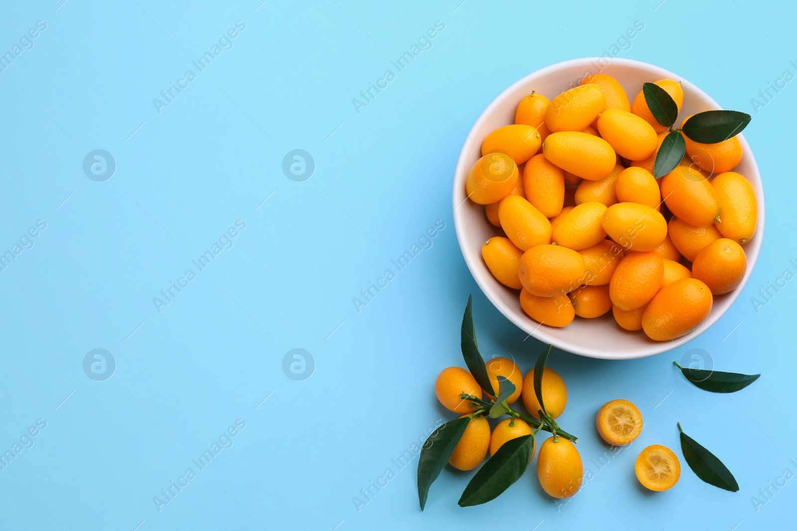 Photo of Fresh ripe kumquats with green leaves on light blue background, flat lay. Space for text