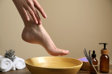 Photo of Woman holding her foot over bowl with water, closeup. Pedicure procedure