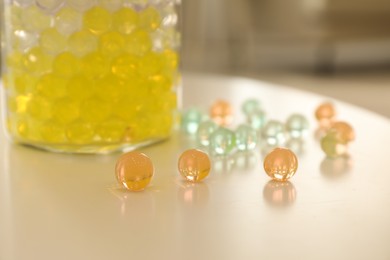 Different color fillers and glass vase on white table in room, closeup. Water beads