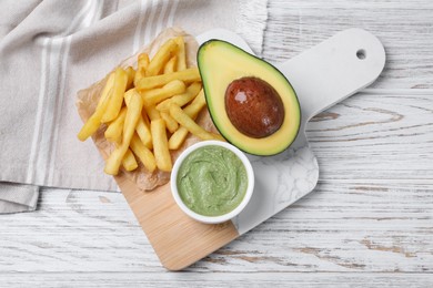 Photo of Serving board with french fries, guacamole dip and avocado on white wooden table, top view