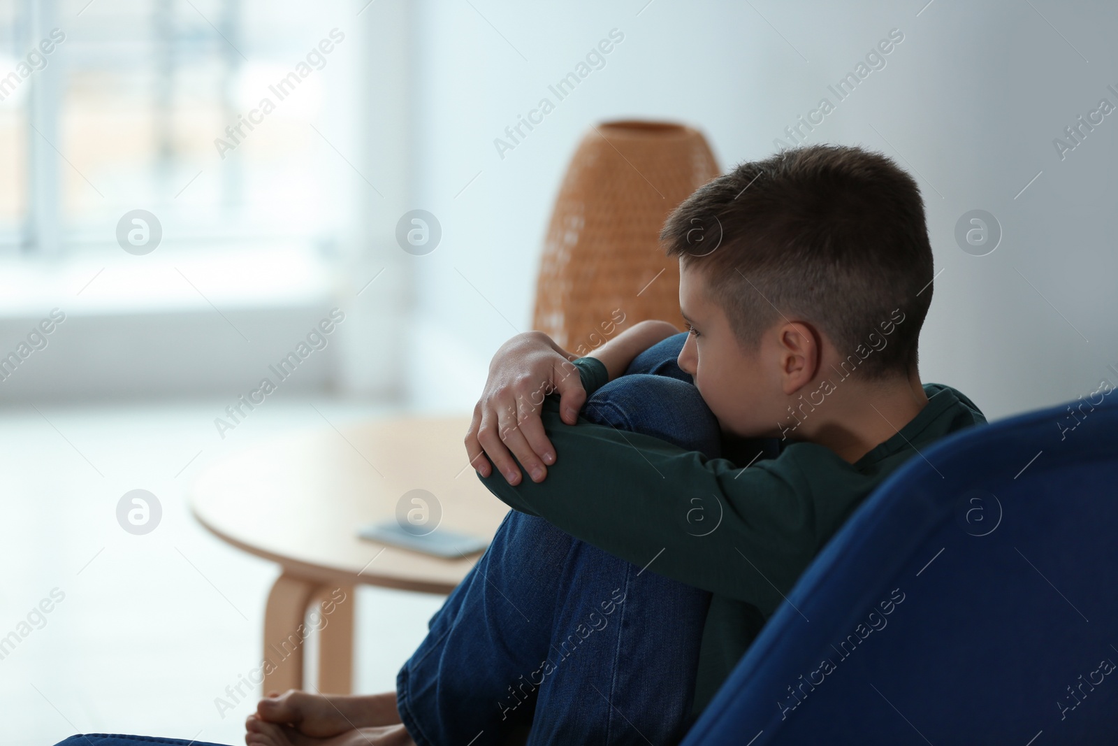 Photo of Upset boy sitting in armchair indoors. Space for text