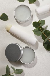 Photo of Different lip balms and leaves on white textured background, flat lay