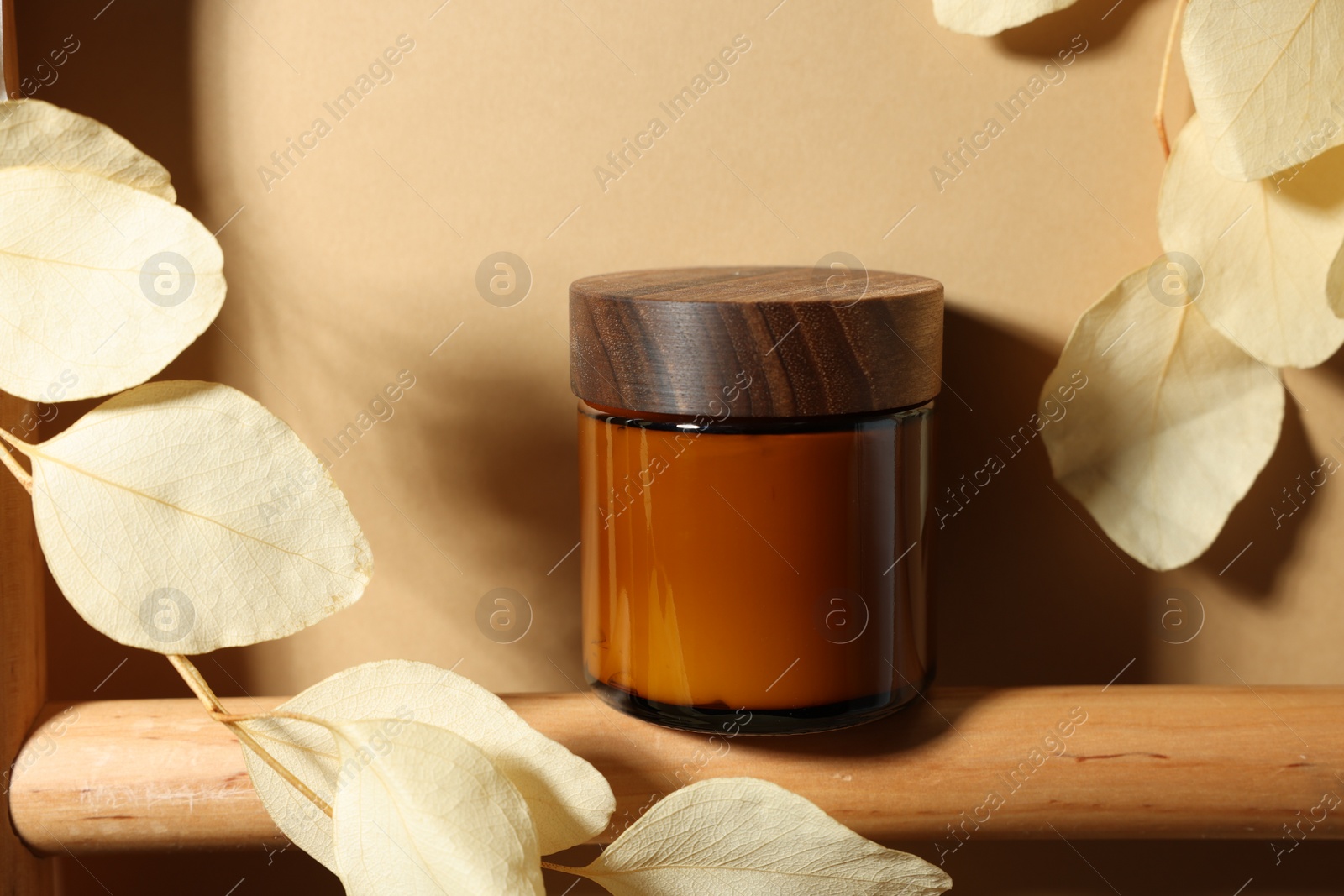 Photo of Jar of luxury cream and dried leaves on dark beige background