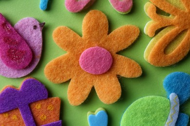 Photo of Different small colorful felt items on green background, flat lay