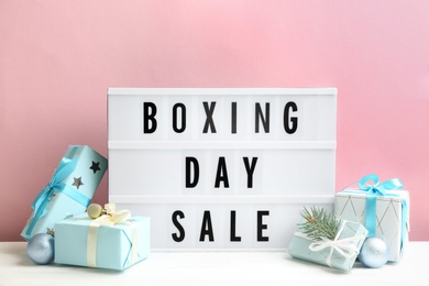 Photo of Composition with Boxing Day Sale sign and Christmas gifts on white table against pink background