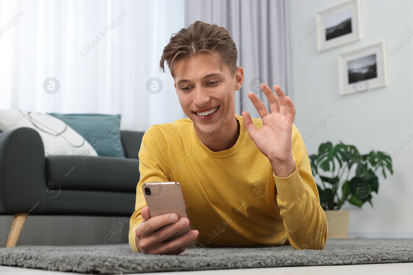 Photo of Happy young man having video chat via smartphone on carpet indoors