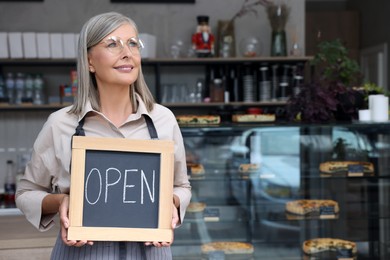 Photo of Happy business owner holding open sign in her cafe, space for text