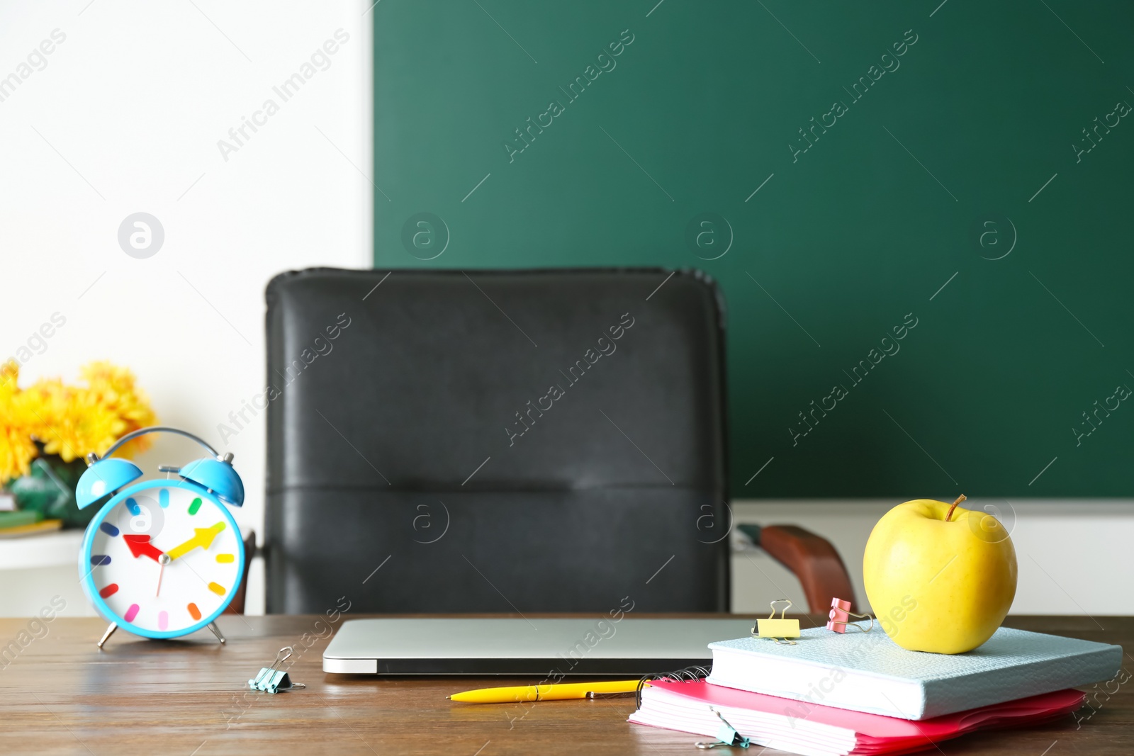 Photo of Laptop, notebooks and alarm clock on table in classroom. Teacher day celebration