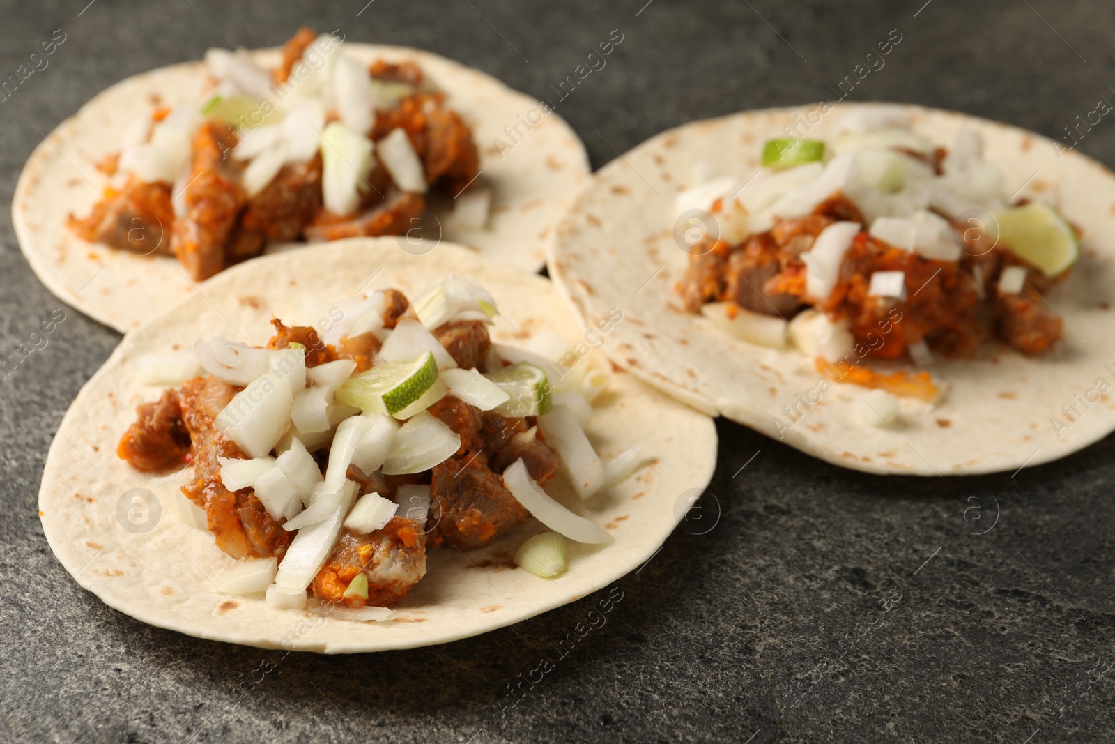 Photo of Delicious tacos with vegetables, meat and lime on grey textured table, closeup