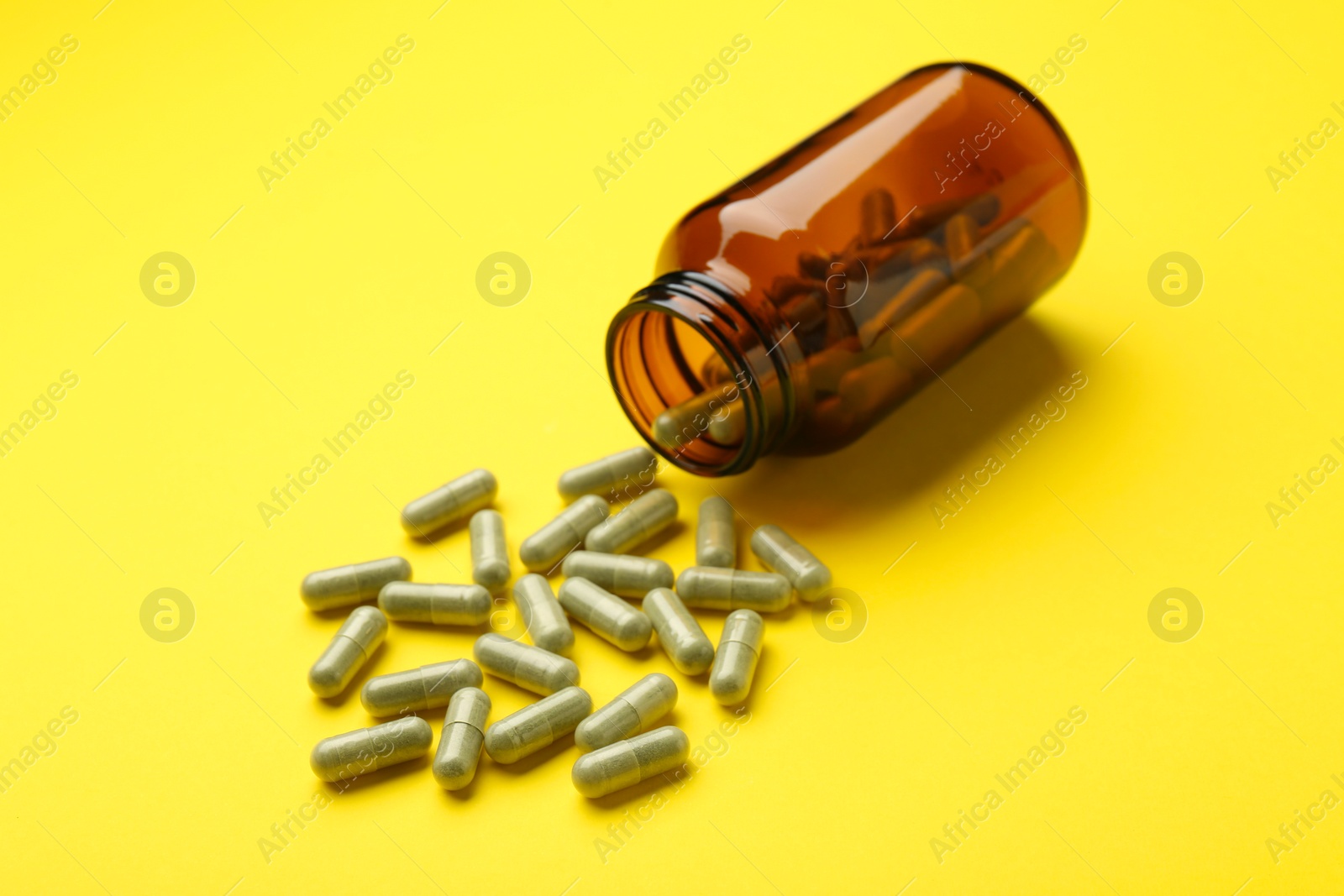 Photo of Vitamin pills and bottle on yellow background, closeup