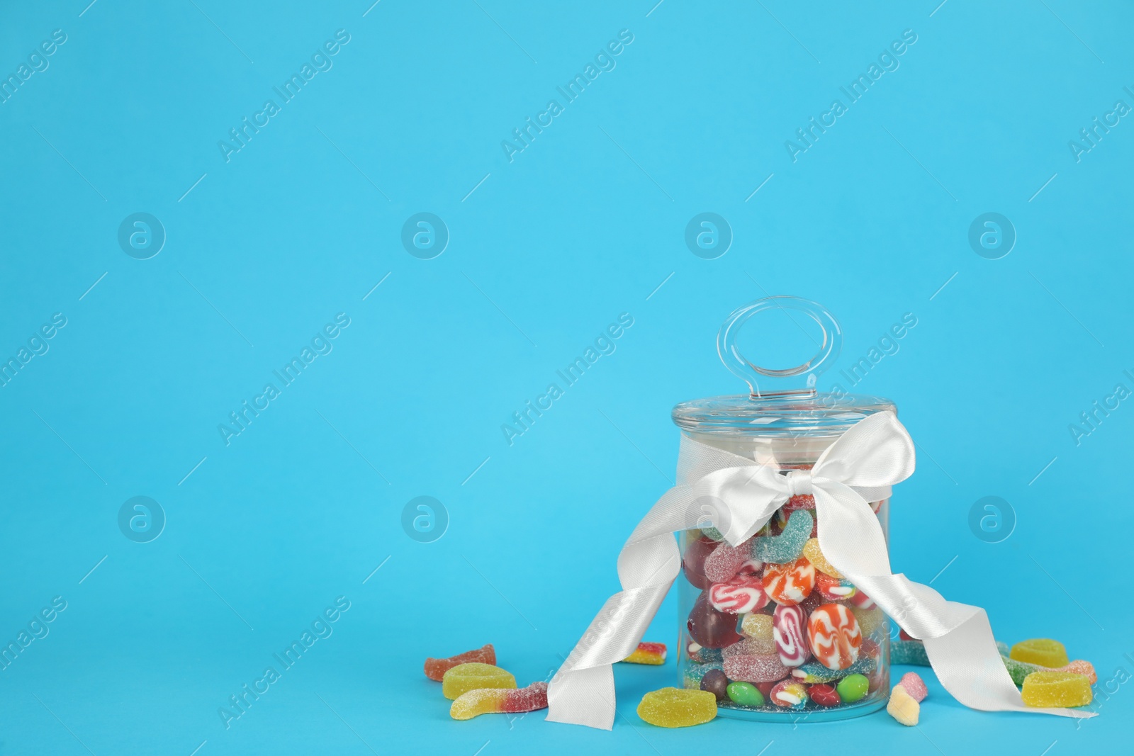 Photo of Glass jar with different candies on light blue background, space for text