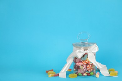 Glass jar with different candies on light blue background, space for text