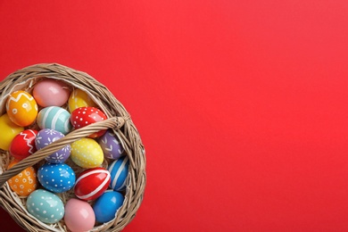 Photo of Wicker basket with painted Easter eggs on color background, top view. Space for text