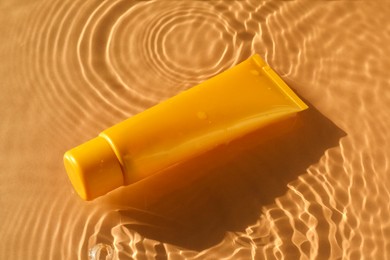 Photo of Tube with moisturizing cream in water on orange background