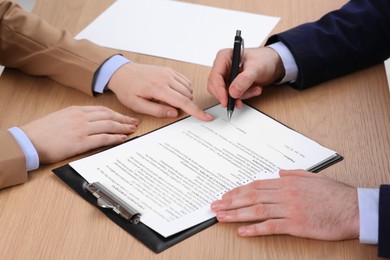 Businesspeople signing contract at wooden table, closeup of hands