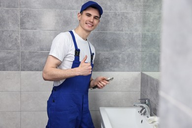 Smiling plumber showing thumb up with spanner in bathroom