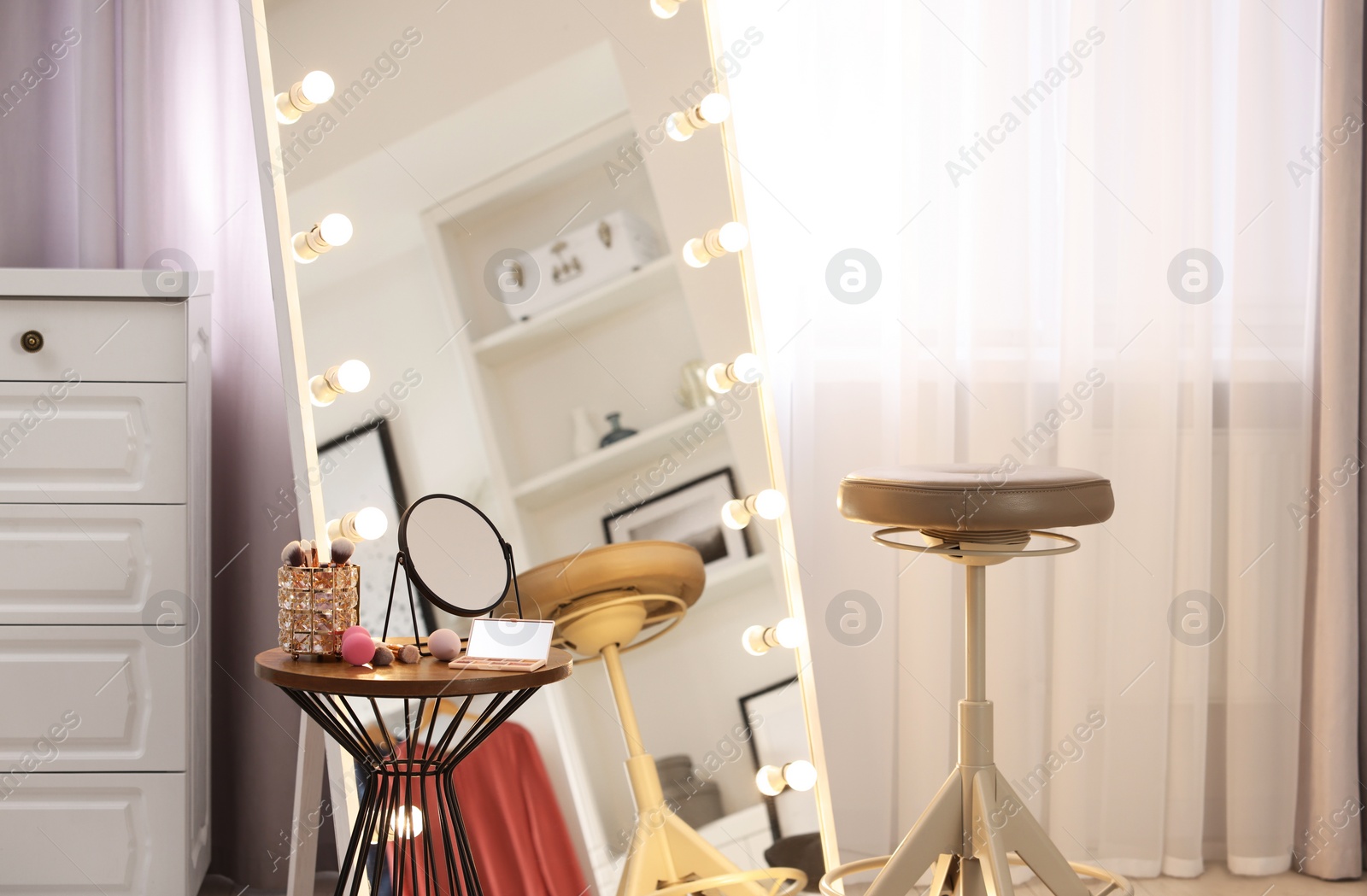 Photo of Makeup room. Stylish mirror with light bulbs, beauty products on table and chair indoors