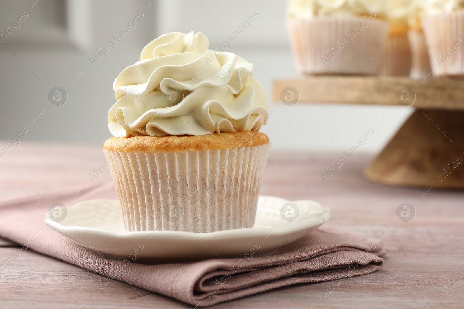 Photo of Tasty cupcake with vanilla cream on pink wooden table, closeup