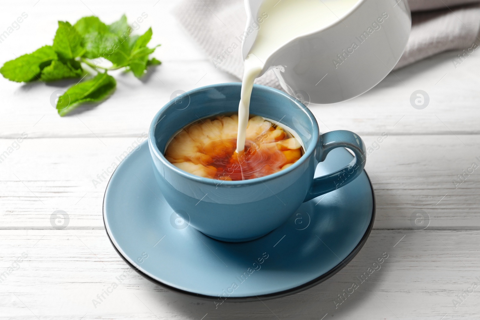 Photo of Pouring milk into cup of black tea on wooden table