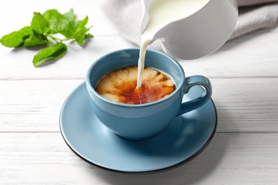 Pouring milk into cup of black tea on wooden table