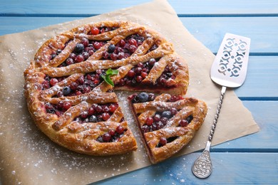 Photo of Delicious cut currant pie with fresh berries and spatula on blue wooden table