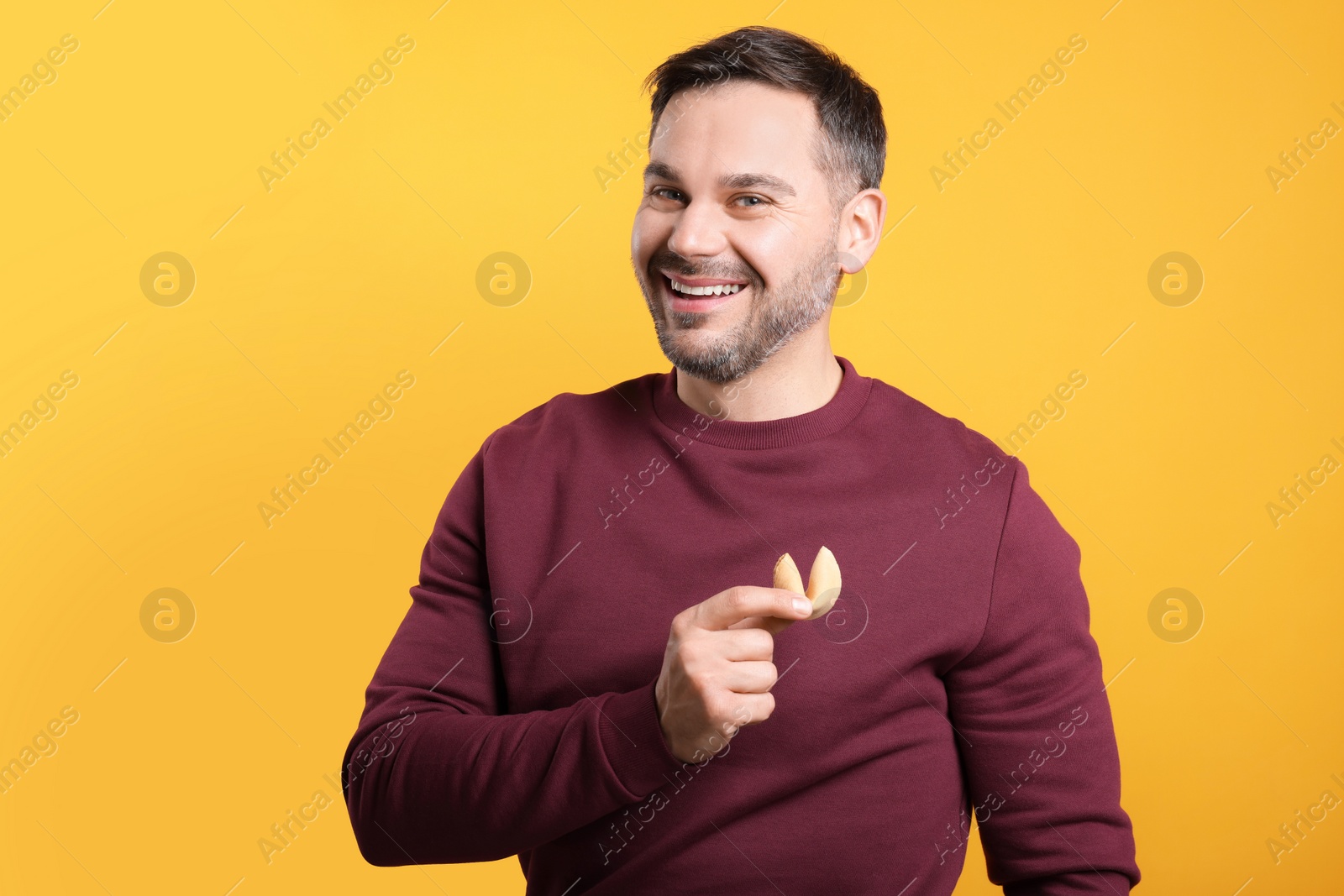 Photo of Happy man holding tasty fortune cookie with prediction on orange background