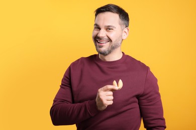 Happy man holding tasty fortune cookie with prediction on orange background