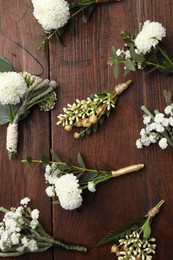 Small stylish boutonnieres on wooden table, flat lay