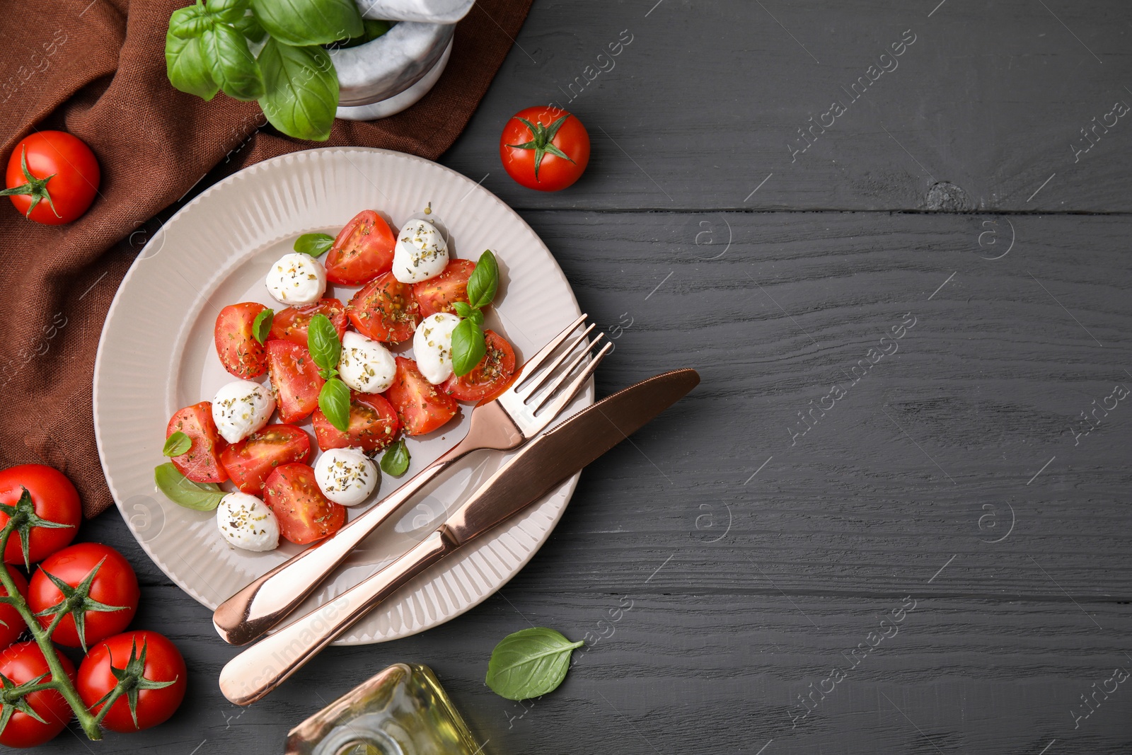 Photo of Tasty salad Caprese with mozarella balls, tomatoes and basil served on grey wooden table, flat lay. Space for text