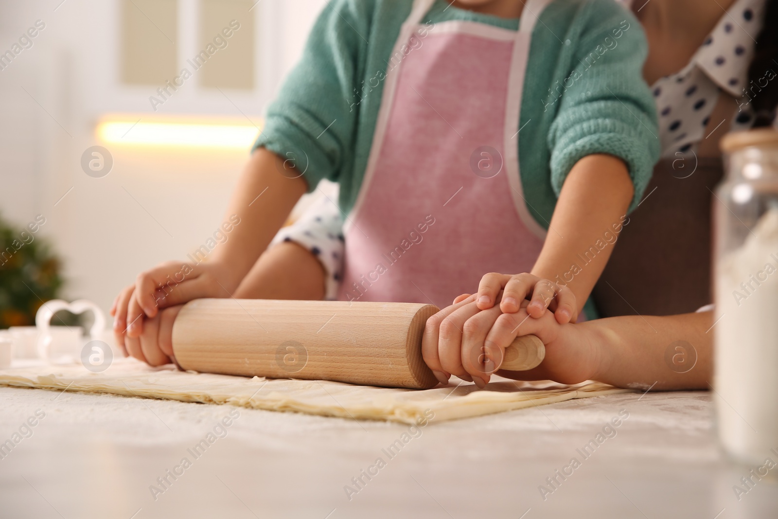 Photo of Mother and daughter rolling out dough in kitchen at home, closeup