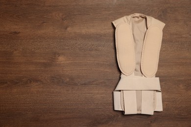 Beige posture corrector on wooden table, top view. Space for text